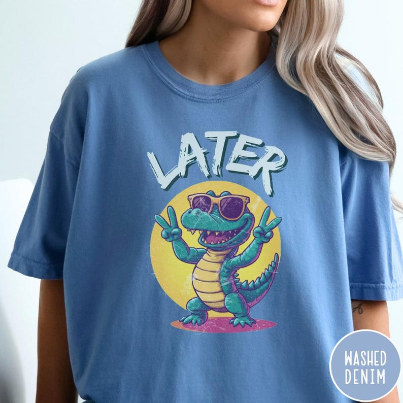 May include: A blue t-shirt with a cartoon alligator wearing sunglasses and the word "LATER" printed on it.