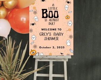 Op de afbeelding: Een Halloween-thema babyshowerbord op een witte ezel. Het bord is perzik van kleur met de tekst "A Little Boo is Almost Due!" en "Welcome to Grey's Baby Shower" met Halloween-thema illustraties. De datum "October 2, 2025" is ook opgenomen.