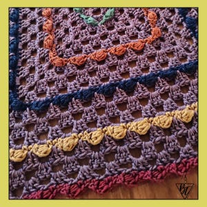 May include: Close-up of a handmade crochet item with a square shape. The piece features a purple base color with decorative borders in orange, navy, yellow, and burgundy. The crochet work has an open, lacy design.