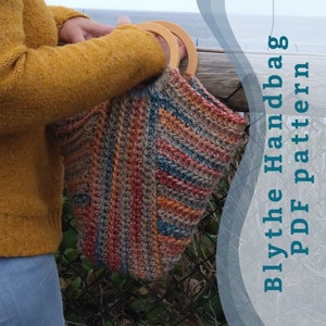 May include: A colorful crocheted handbag with wooden handles. The bag is being held by a person wearing a yellow sweater and blue jeans. The text "Blythe Handbag PDF Pattern" is in the background.