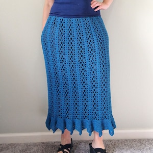 May include: A long, teal blue crochet skirt with a scalloped hem. The skirt is made with a delicate open stitch pattern.
