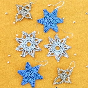 May include: Six crocheted earrings in the shape of stars and a flower. Two of the earrings are blue, two are silver, and two are gold.