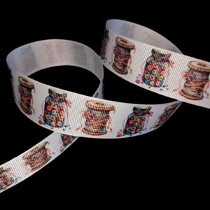 May include: White ribbon with a repeating pattern of vintage-style jars filled with colorful buttons and spools of thread. The ribbon is curled and has a slight sheen, perfect for crafting and sewing projects.