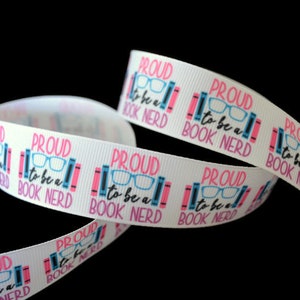 May include: White ribbon with the text "PROUD to be a BOOK NERD" in pink and blue. The design includes glasses and books. The ribbon is curled against a black background.
