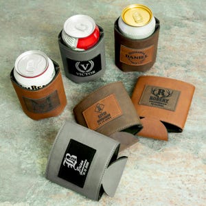 May include: Six personalized leather can coolers in gray and brown with different names and titles, such as "Groom", "Best Man", and "Groomsman".