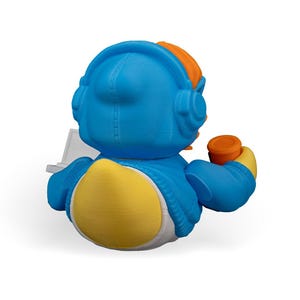 May include: A blue rubber duck wearing a blue hoodie with a white zipper and orange headphones. The duck is holding a white laptop and a cup of coffee in its right hand.