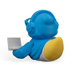 May include: A blue and yellow 3D printed duck wearing headphones and holding a laptop.