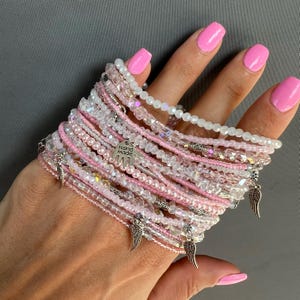 May include: A stack of pink and clear beaded bracelets with silver charms, including a charm that says "Hand Made".