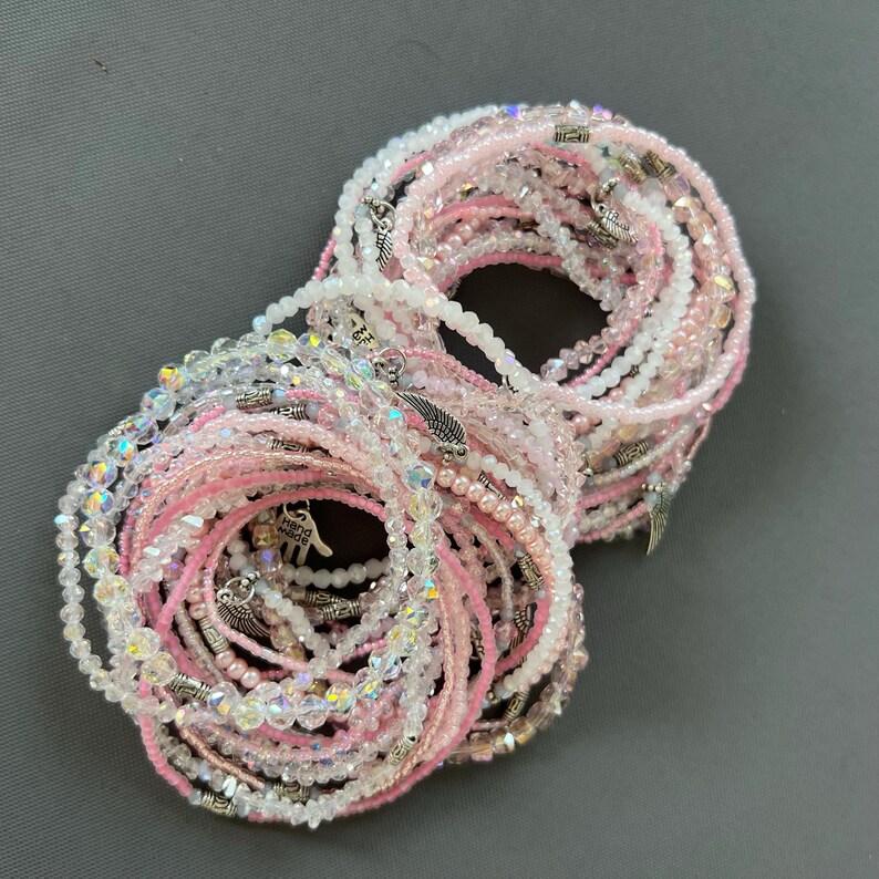 May include: A set of pink and clear beaded bracelets with silver charms. The bracelets are stacked on top of each other and are ready to be worn.