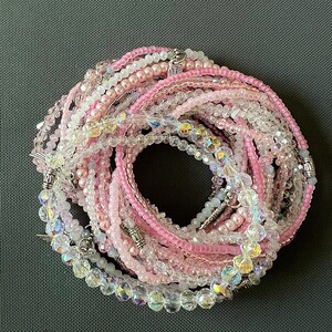 May include: A set of pink and clear crystal beaded bracelets with silver accents. The bracelets are layered and arranged in a circle.