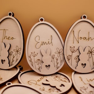 Peut inclure: Six d&eacute;corations d'&oelig;ufs de P&acirc;ques en bois avec des silhouettes de lapins et des noms personnalis&eacute;s&nbsp;: Th&eacute;o, Emil, No&eacute;, Emma, Paul et Lisa. Les d&eacute;corations sont d&eacute;coup&eacute;es au laser et ont une finition en bois naturel.
