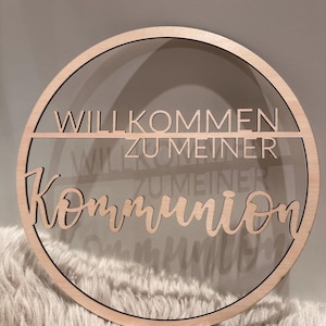 Könnte beinhalten: Ein Holz-Kreis mit dem Text "Willkommen zu meiner Kommunion" in einer kursiv geschriebenen Schrift. Der Text ist aus dem Holz ausgeschnitten und der Hintergrund ist aus klarem Acryl.