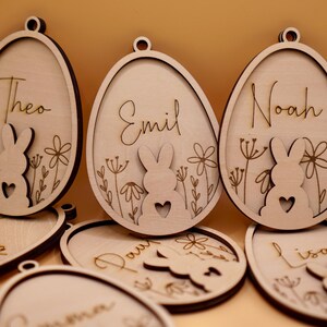 Peut inclure: Ornements d'&oelig;ufs de P&acirc;ques en bois avec des silhouettes de lapins et des noms personnalis&eacute;s, notamment Theo, Emil, Noah, Emma, Paul, Lisa et Carmen.