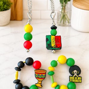 May include: Two beaded lanyards and two beaded bracelets featuring red, yellow, green, and black silicone beads. One lanyard has a Black History Month charm, the other has round beads. One bracelet features a chalice charm, the other a God Is My Strength charm.