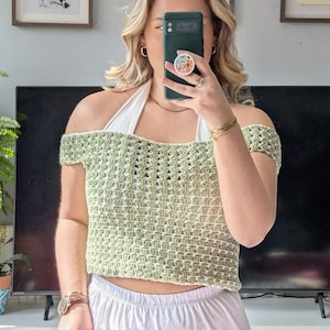 Peut inclure: Haut en crochet vert clair et blanc avec des manches épaules nues. Le haut présente un motif ajouré. Les bretelles sont blanches. Le haut est associé à un pantalon blanc.