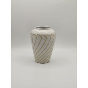 May include: A white ceramic vase with a grey rim and a rounded body. The vase is decorated with diagonal, gold-coloured, wavy lines. The vase has a smooth, glossy finish and is set against a plain white background.