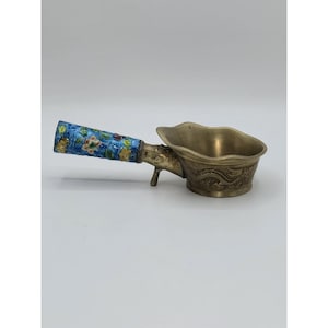 May include: A vintage metal tea scoop with a blue floral enamel handle and a brass-colored bowl. The bowl features a dragon design. The scoop is designed with a small spout and a handle for easy use.