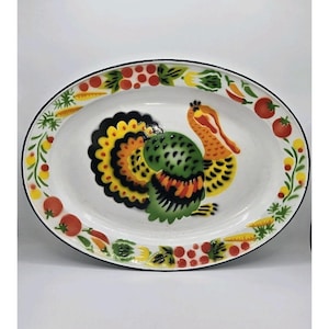 Puede incluir: Plato ovalado blanco con un diseño de pavo colorido. El pavo presenta detalles verdes, amarillos, naranjas y negros. El borde está decorado con tomates rojos, hojas verdes y zanahorias amarillas. El plato tiene un borde negro.
