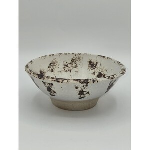 May include: A white ceramic bowl with a speckled brown pattern around the rim and interior. The bowl has a rounded shape and a light beige base. The speckled design adds a rustic touch to the bowl's appearance.