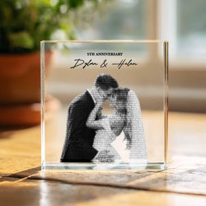 Peut inclure: Un bloc de verre transparent rectangulaire avec une image en noir et blanc d'un couple. Le texte "5TH ANNIVERSARY" et les noms "Dylan & Helen" sont imprimés. Posé sur une surface en bois.