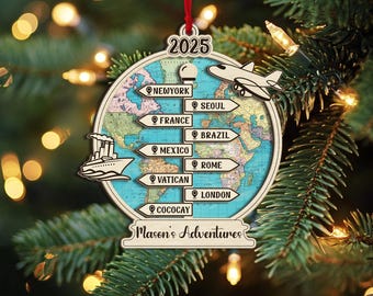 以下が含まれることがあります： 世界地図のデザインが施された木製のクリスマスオーナメント。旅行先と2025年が描かれています。「Mason's Adventures」の文字と船と飛行機のグラフィックが含まれています。赤いリボンで吊り下げられています。
