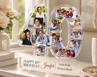 May include: A clear acrylic photo display in the shape of the number 40, filled with multiple photos. The base reads "HAPPY 40TH BIRTHDAY Jenifer Love from Olivia & Noah". The display is on a white surface with a vase of flowers in the background.