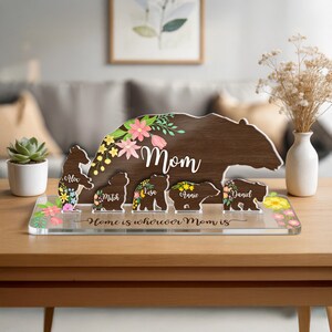 May include: A wooden bear-shaped sign with the word "Mom" and floral accents. The sign includes smaller bear figures with names, set on a clear base with the text "Home is wherever Mom is."