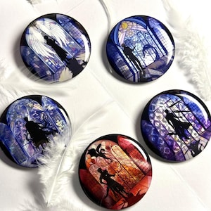 May include: Five circular pin badges with stained glass designs. Each badge features a silhouette of a person or figures against a backdrop of vibrant colours, including blues, purples, and reds. White feathers are scattered around the badges.