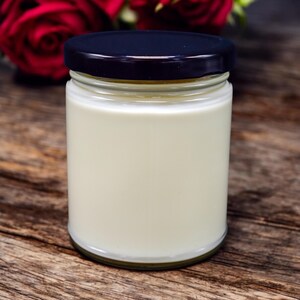 Puede incluir: Una vela blanca en un tarro de vidrio transparente con tapa negra. El tarro est&aacute; sobre una superficie de madera.