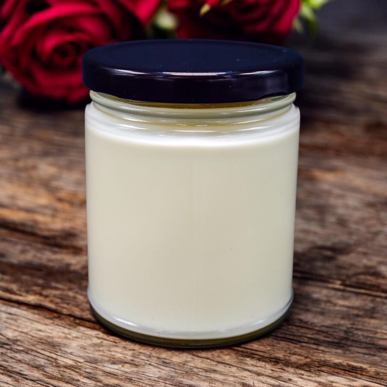 Puede incluir: Una vela blanca en un tarro de vidrio transparente con tapa negra. El tarro est&aacute; sobre una superficie de madera.