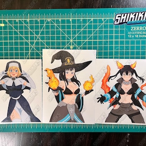 May include: Three anime-style character prints on a green cutting mat. The prints feature female characters in various outfits, including a nun, a witch, and a character with fire-themed elements. The cutting mat measures 12 x 18 inches.
