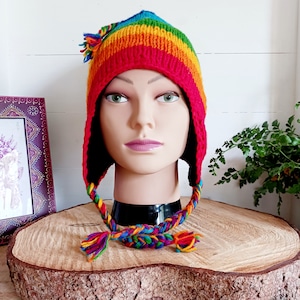 Peut inclure: Un bonnet tricoté rayé arc-en-ciel avec un long cordon tressé. Le bonnet a une base rouge et est surmonté d'un arc-en-ciel de couleurs, dont le jaune, l'orange, le vert, le bleu et le violet. Le cordon est tressé avec les mêmes couleurs que le bonnet.