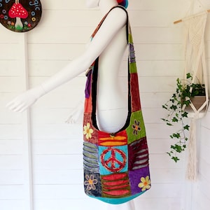 May include: A colourful patchwork shoulder bag with a peace sign and floral embroidery. The bag is made of different fabrics and has a long strap.