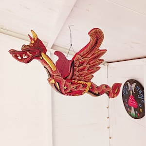 May include: A red and gold wooden dragon sculpture with wings hanging from the ceiling. The dragon is painted with intricate details and has a fierce expression.