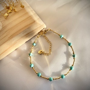 May include: A gold chain anklet with turquoise beads. The anklet has a small heart charm and an adjustable clasp.