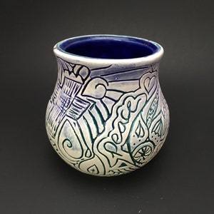May include: A white ceramic vase with a blue and green abstract design. The vase has a rounded bottom and a wide opening.