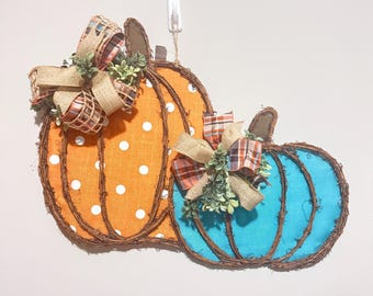 May include: A decorative pumpkin-shaped wall hanging. One pumpkin is orange with white polka dots, the other is turquoise. Both have brown vine outlines, brown fabric stems, and burlap and plaid bows with greenery.