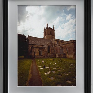 Moody sky over a old gothic church in England. Path leading to door in front of graves with flowers.