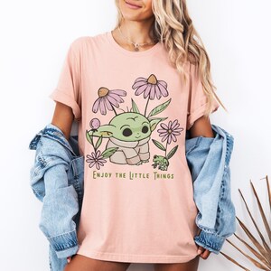 a woman wearing a pink t - shirt with a picture of a baby yoda