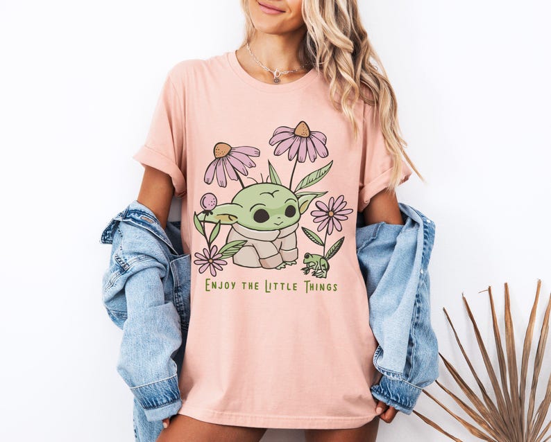 a woman wearing a pink t - shirt with a picture of a baby yoda