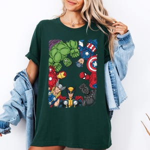 A woman wearing a green t-shirt with a graphic of various Marvel superheroes, including Hulk, Spider-Man, Captain America, and others, standing together.