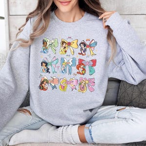a woman sitting on a couch wearing a sweatshirt with cartoon characters on it