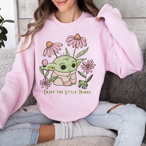 a woman sitting on a couch wearing a pink shirt with a baby yoda on