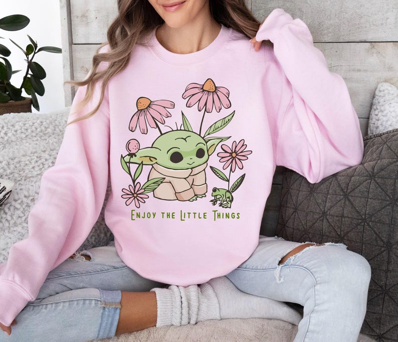 a woman sitting on a couch wearing a pink shirt with a baby yoda on