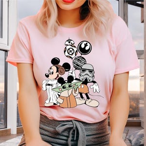 May include: Pink t-shirt with a graphic print of Mickey Mouse, Yoda, and a Stormtrooper holding balloons. The balloons are shaped like the Death Star, a TIE fighter, and a character from Star Wars.