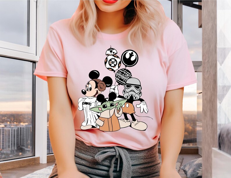 May include: Pink t-shirt with a graphic print of Mickey Mouse, Yoda, and a Stormtrooper holding balloons. The balloons are shaped like the Death Star, a TIE fighter, and a character from Star Wars.