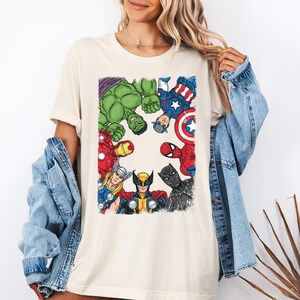 A woman wearing a white t-shirt with a graphic of various Marvel superheroes, including Hulk, Captain America, Spider-Man, and others, standing in a circle.
