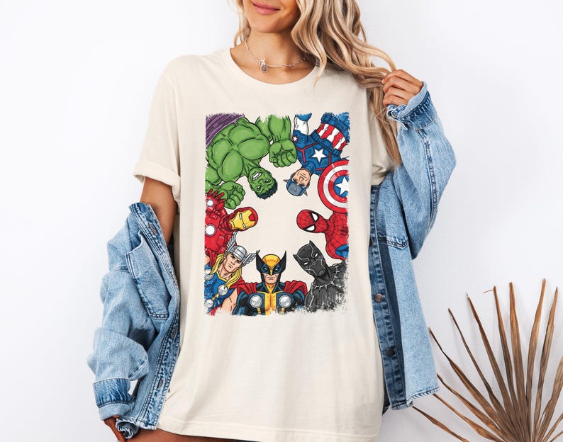 A woman wearing a white t-shirt with a graphic of various Marvel superheroes, including Hulk, Captain America, Spider-Man, and others, standing in a circle.