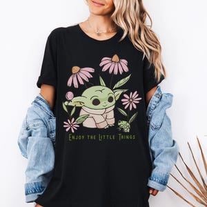 a woman wearing a black t - shirt with a picture of a baby yoda