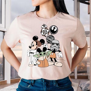 May include: A pink t-shirt with a graphic print of Mickey Mouse, Yoda, and a Stormtrooper holding balloons. The balloons are shaped like the Death Star, a TIE fighter, and a BB-8 droid.